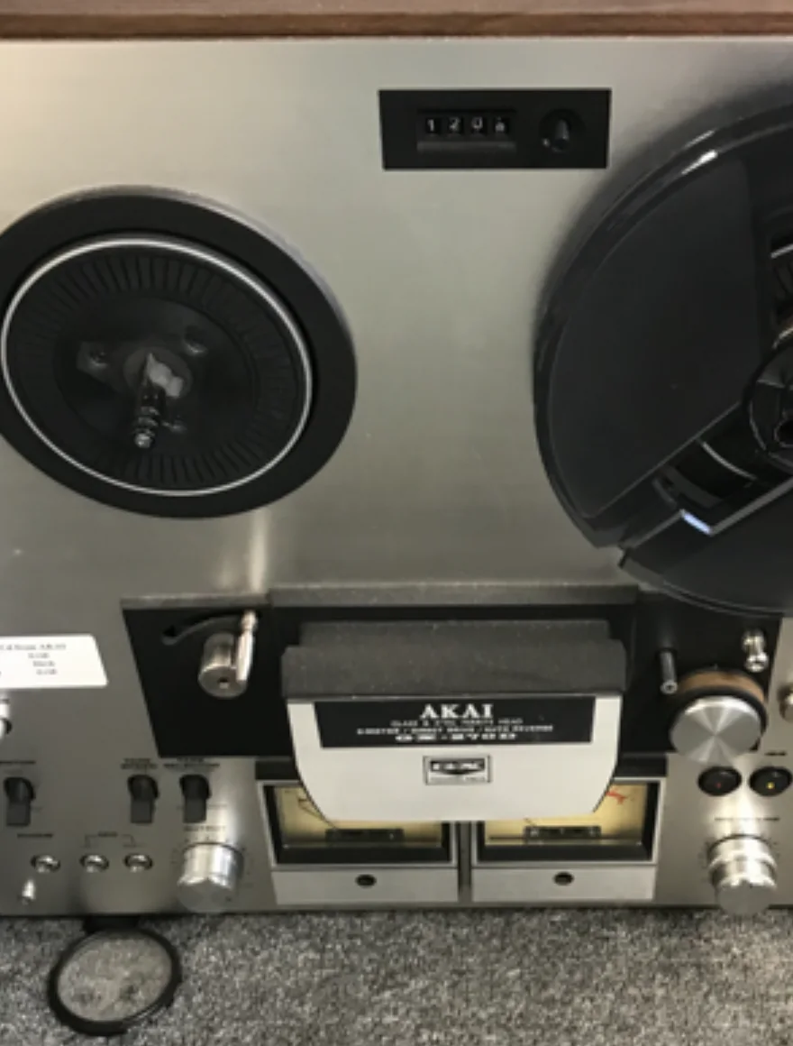 Akai reel-to-reel tape recorder with reels, level meters, and front controls.
