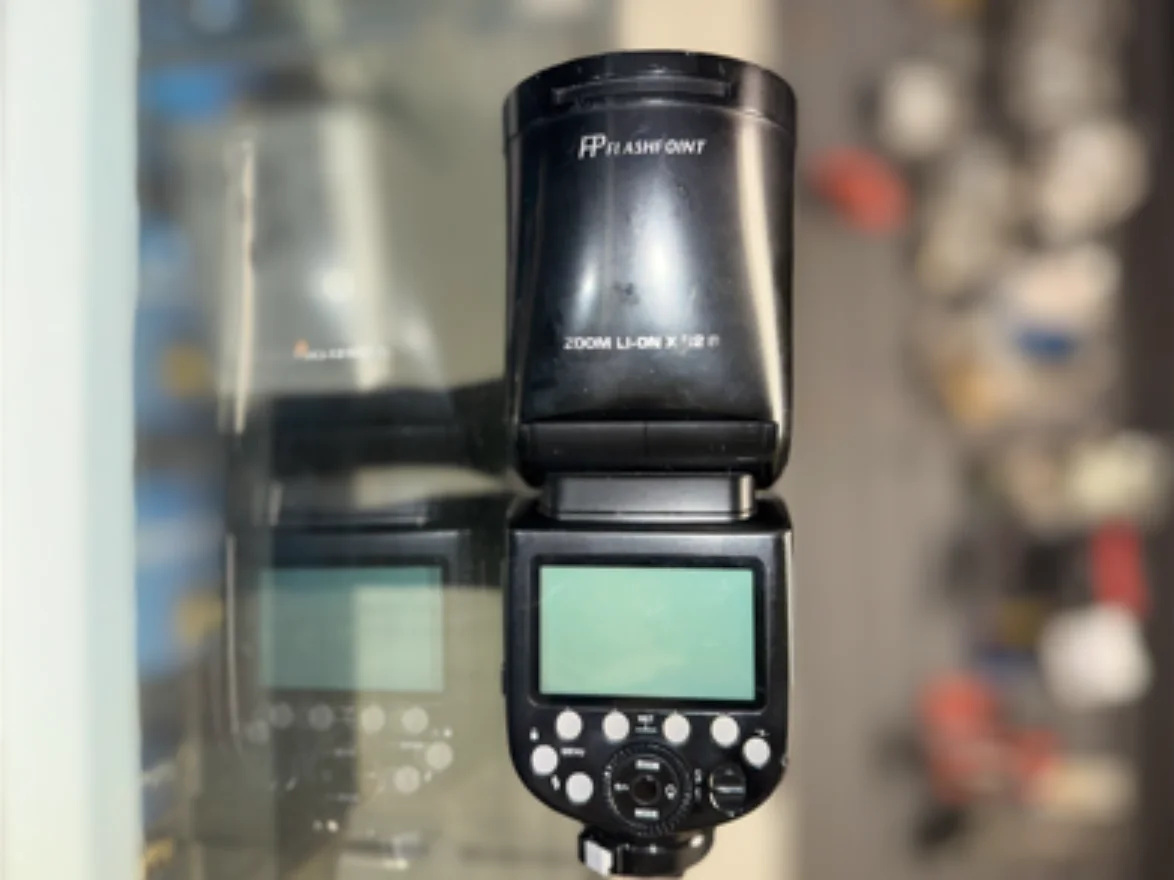 External camera flash with a digital display and control buttons on a glass counter.