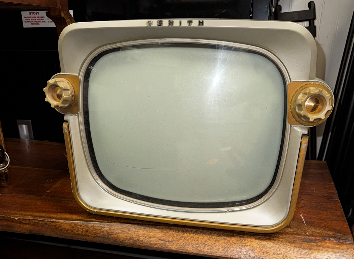 Cream and gold Zenith television on a wooden shelf.
